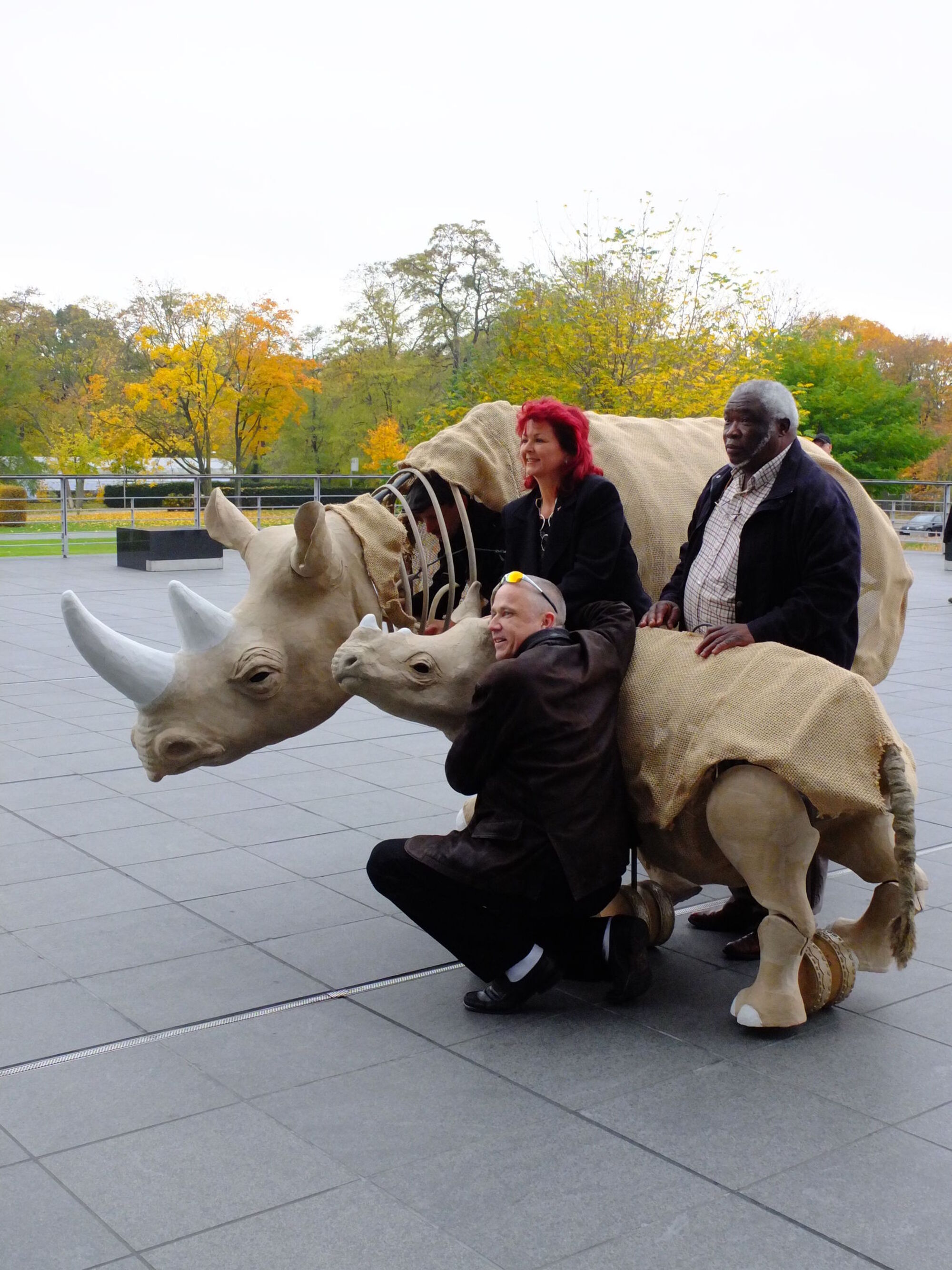 Drei Personen lassen sich fotografieren mit zwei Nashorn-Skulpturen.