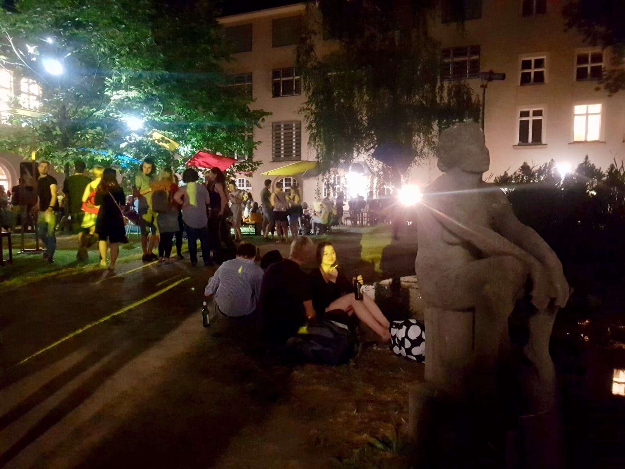 Innenhof der Hochschule an der Güntzstraße in der Nacht. Menschen unterhalten sich während des Sommerfestes. Gartenskulptur von einer Frau im Vordergrund.