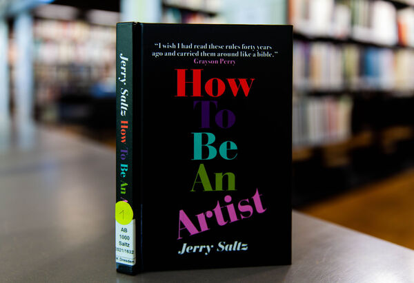 Wie man ein Künstler wird (How to be an artist) Das Buch "Wie man ein Künstler wird" auf einem Tisch, im Hintergrund Bücherregale der Bibliothek