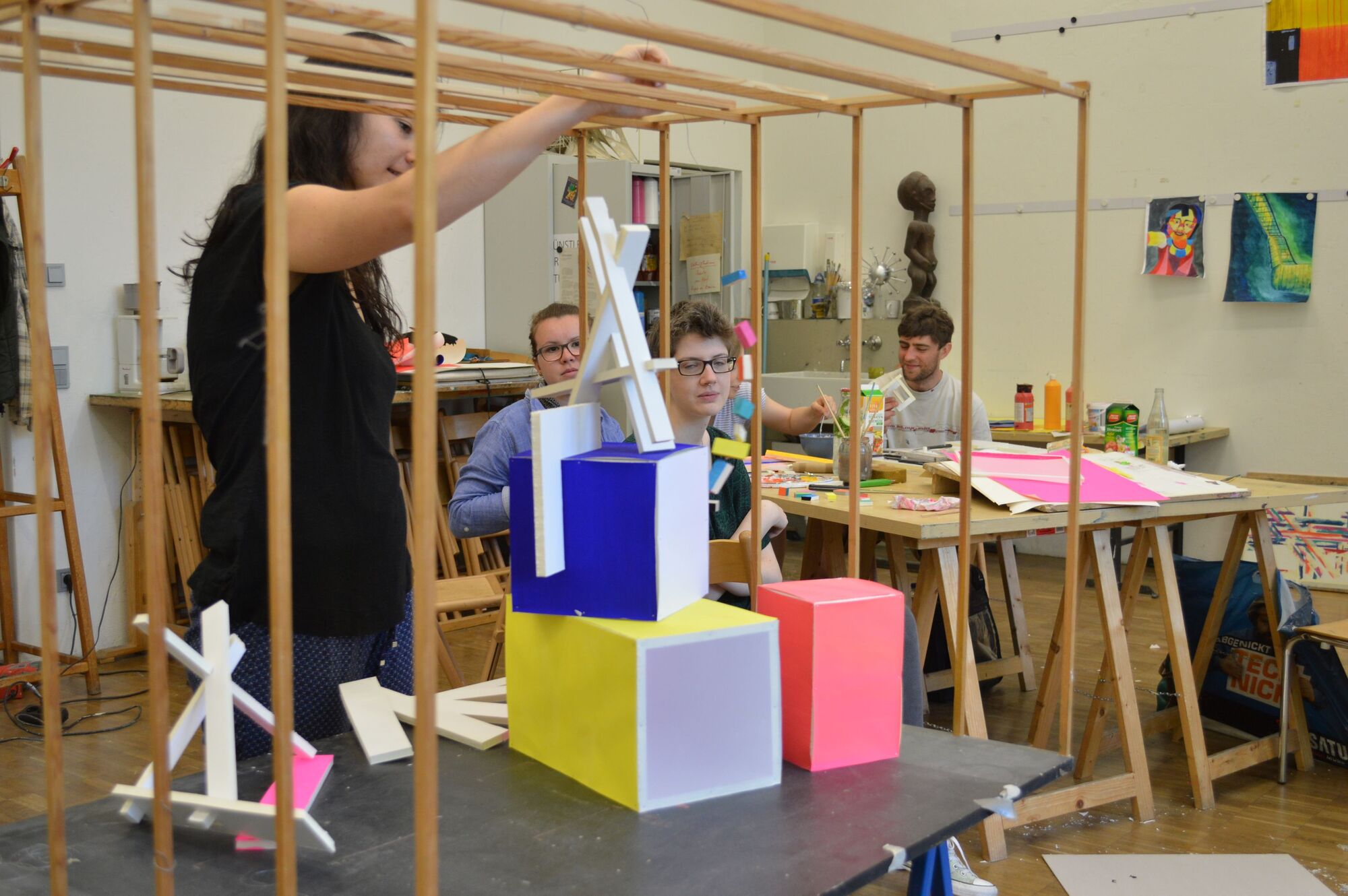 Studenten in dem Atelier. Eine Studentin macht eine Gestaltung aus geometrischen, bunten Objekten.