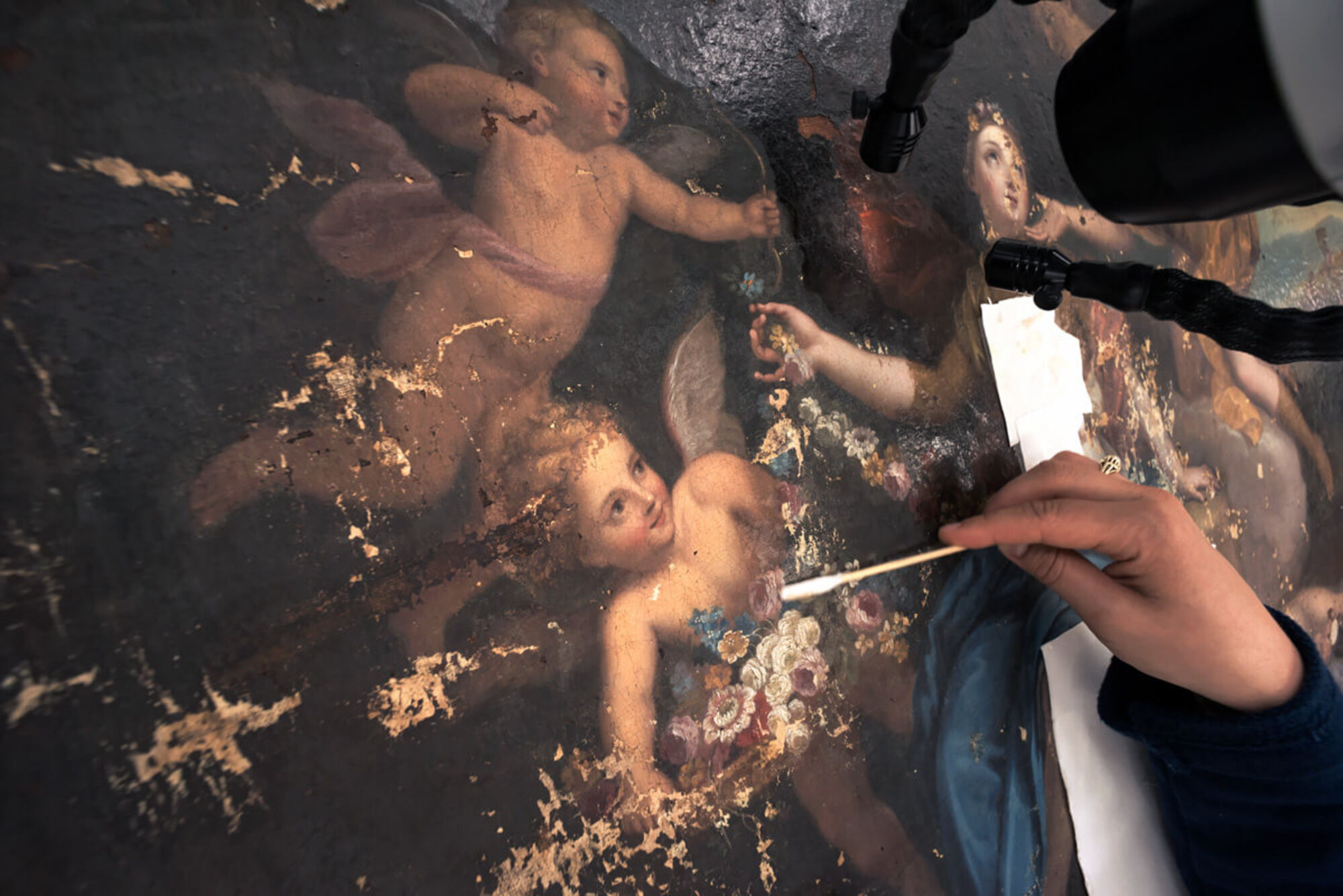 Das Restaurieren eines Gemäldes. Auf dem Gemälde sieht man zwei Engel.