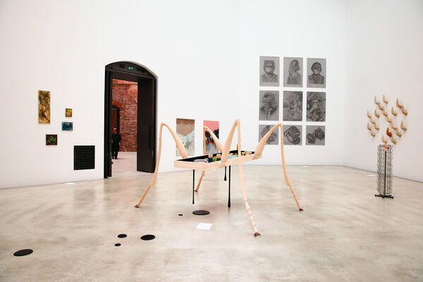 Ausstellungsansicht: Bilder an der Wand und eine große Holzskulptur.