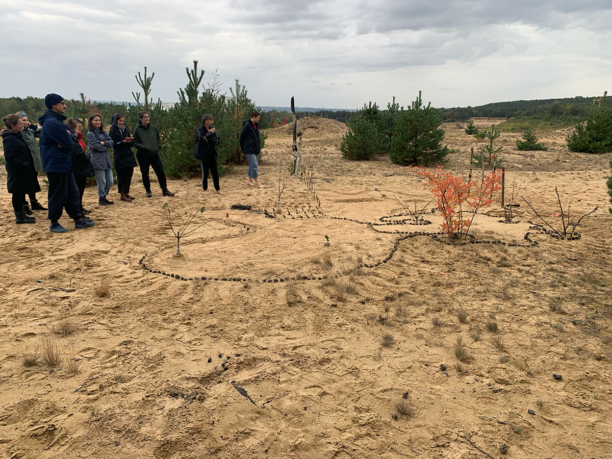 Studierende stehen um ein mit Naturmaterialien gelegtes Muster herum.