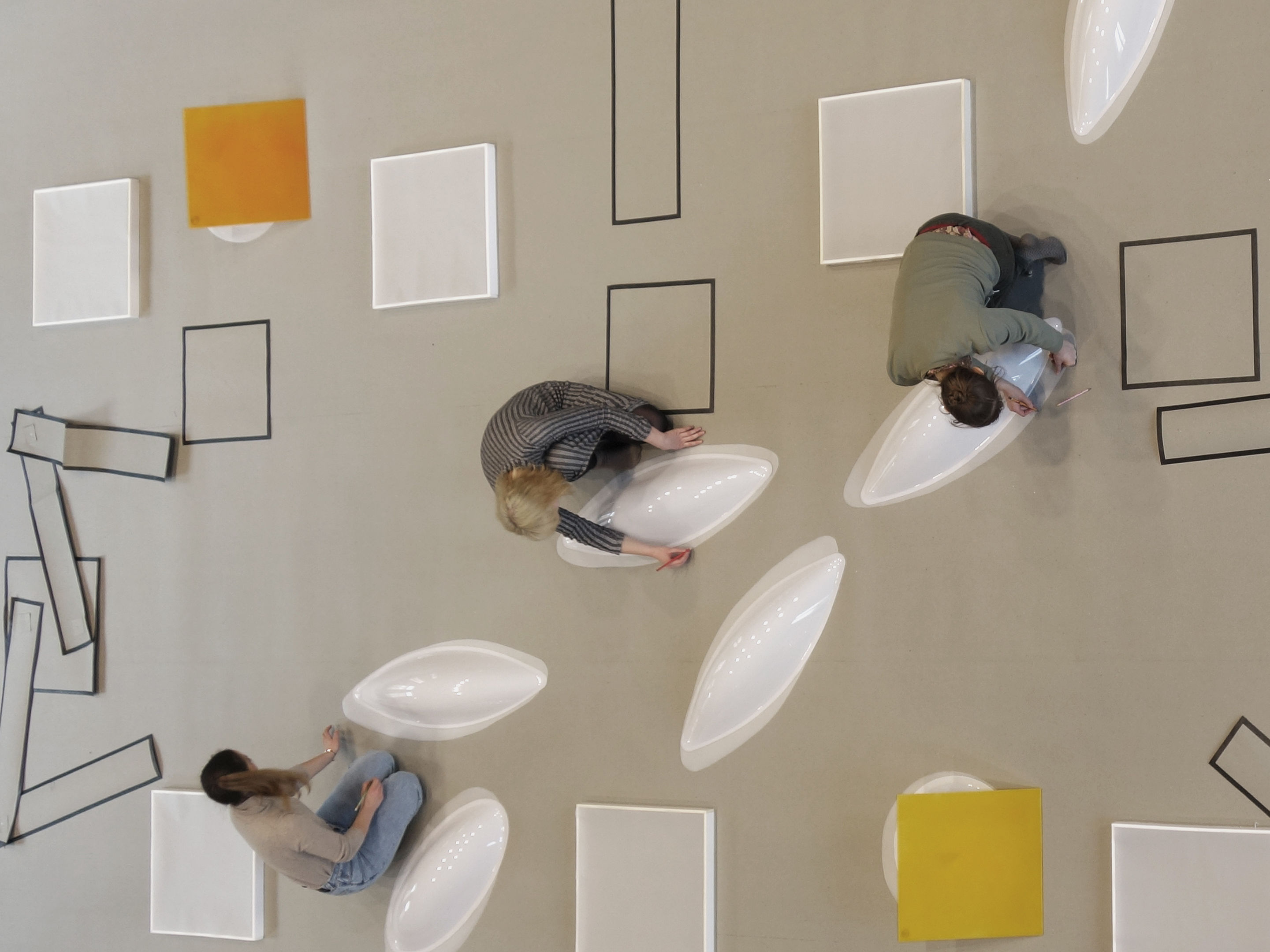 Blick von oben auf den Boden. Drei Studentinnen zeichnen geometrische Formen und arrangieren große geometrische Objekte auf dem Boden.