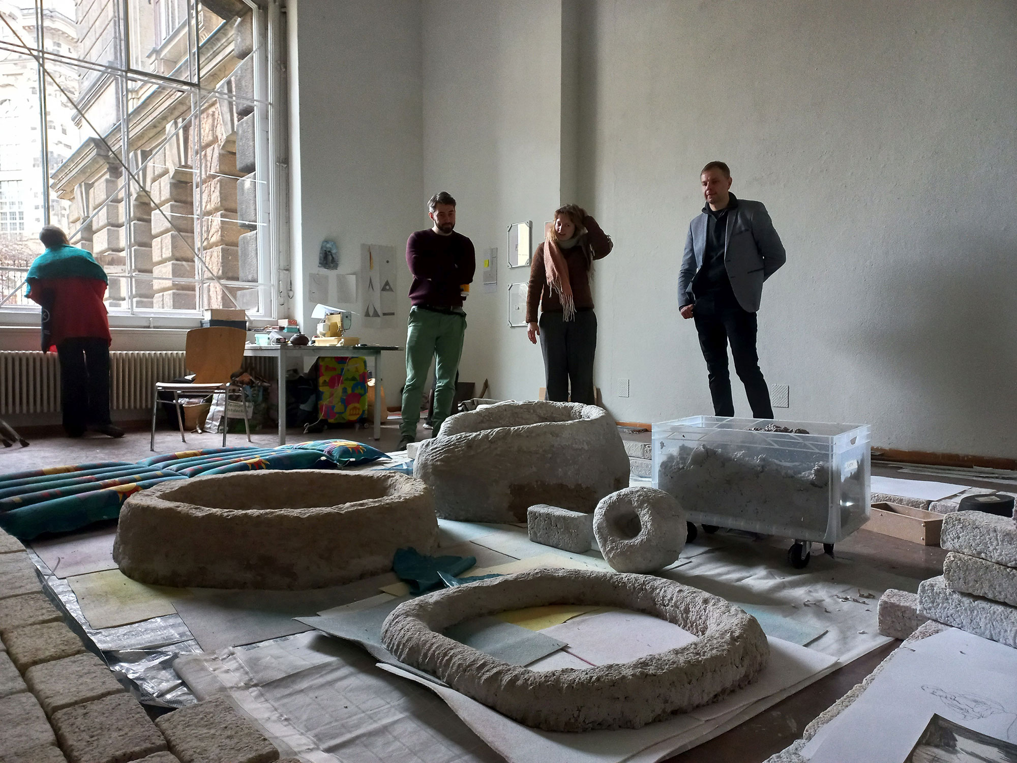 Studio visit. People stand around a work lying on the floor.