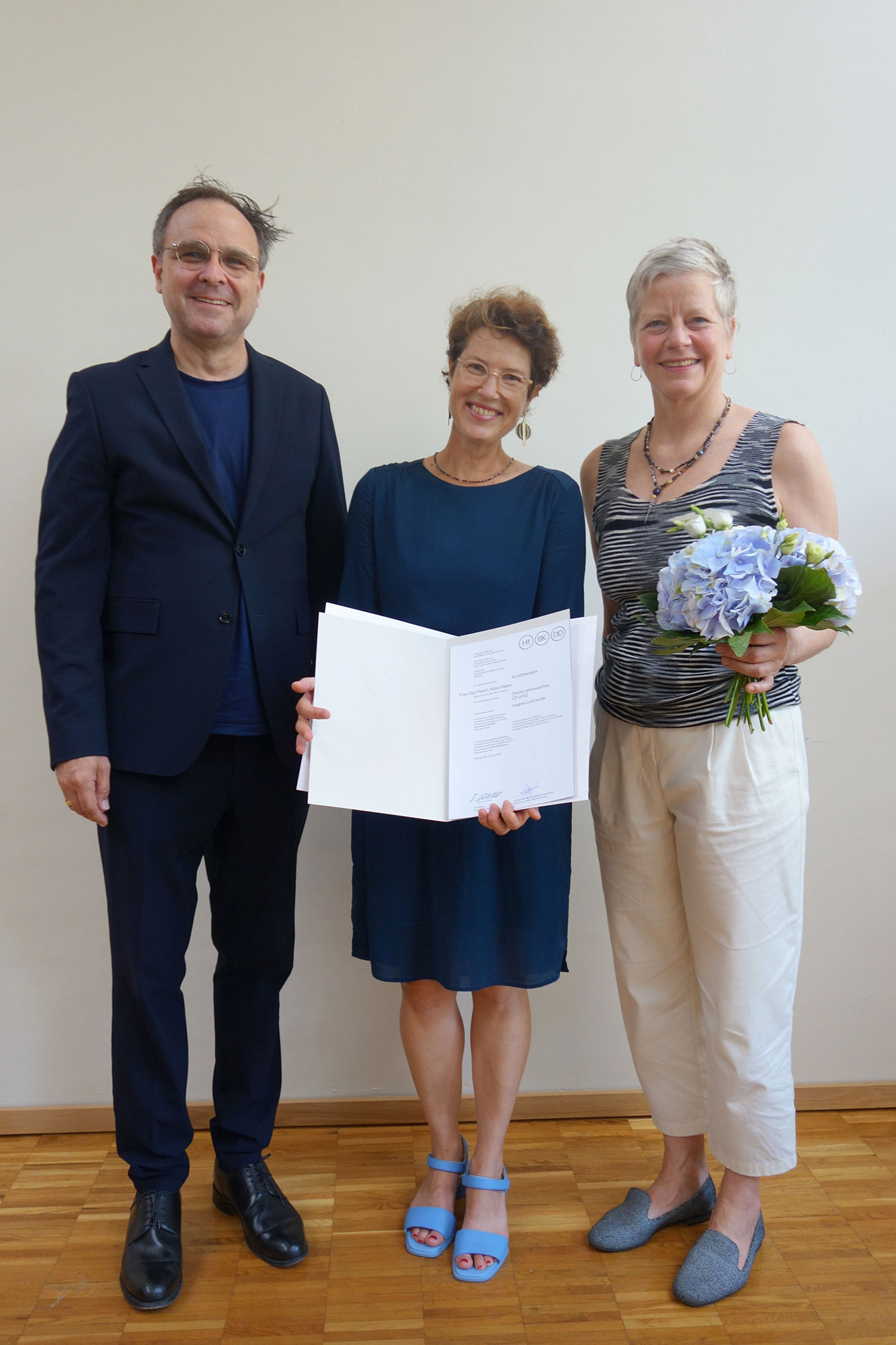 Drei Personen, die mittlere hält ein Zeugnis in der Hand. Drei Personen, die mittlere hält ein Zeugnis in der Hand.