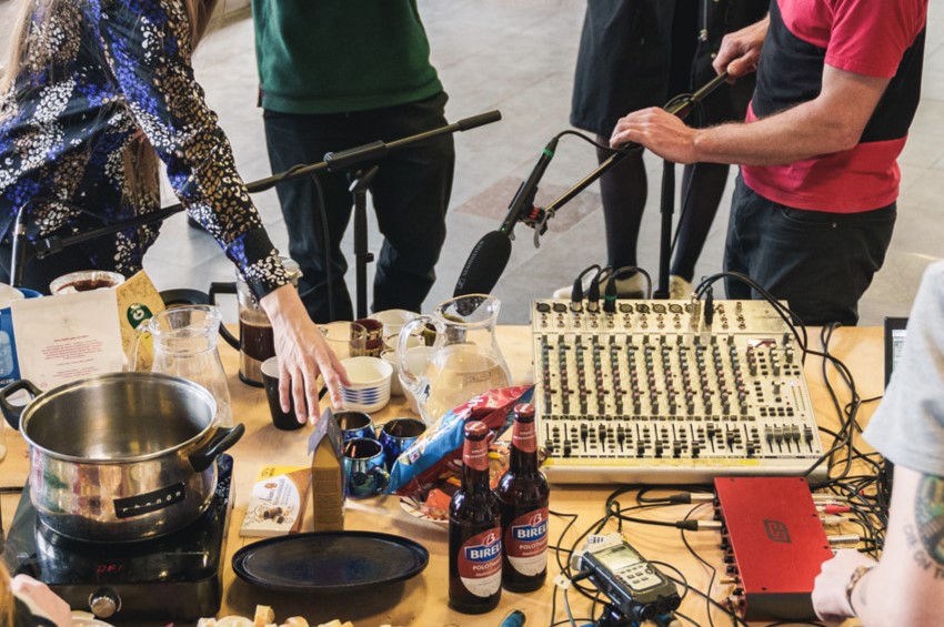 Ein Mischpult auf einem Tisch. Menschen stehen darum herum