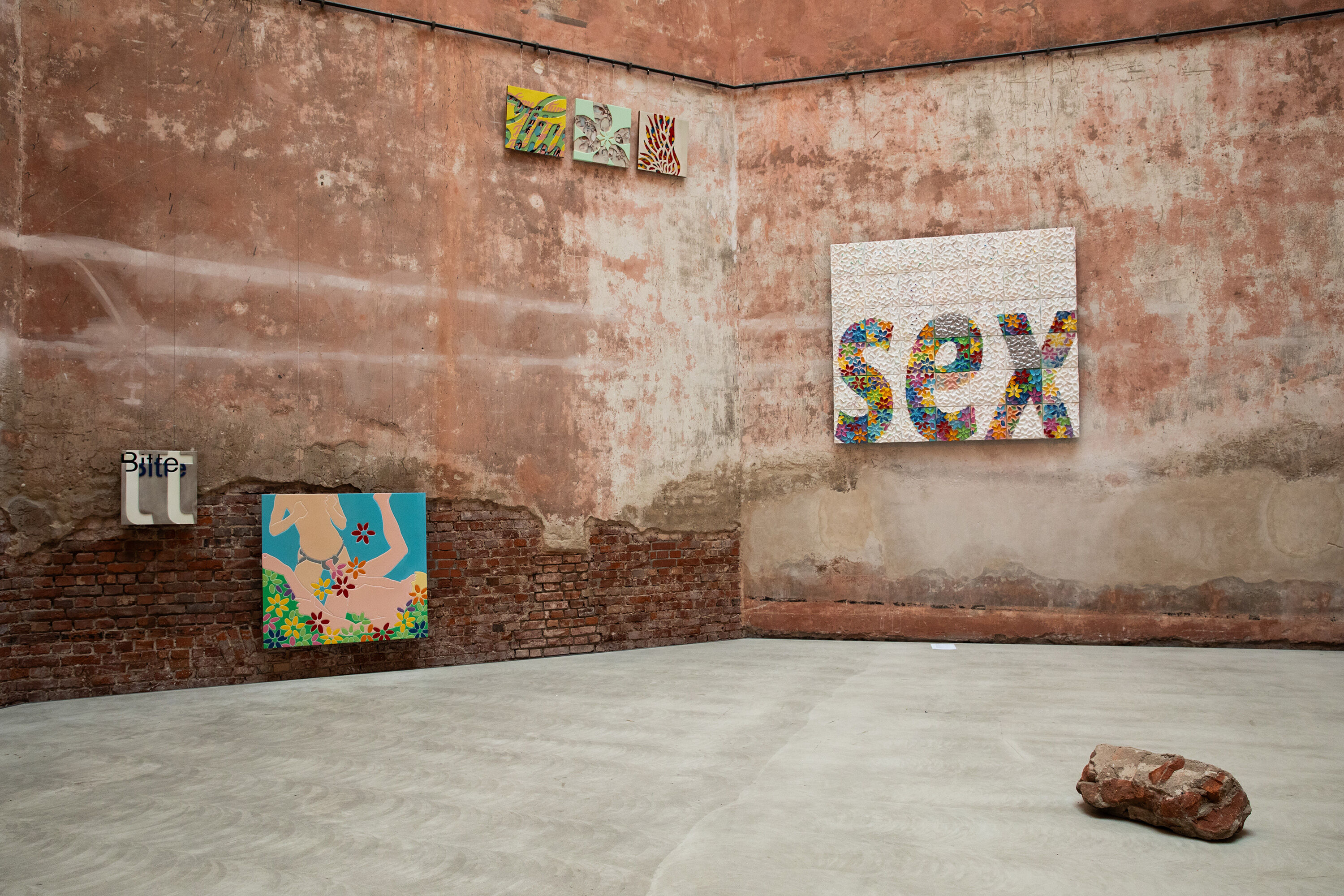 Ausstellungsansicht, verschiedengroße Bilder an einer roten Backsteinwand